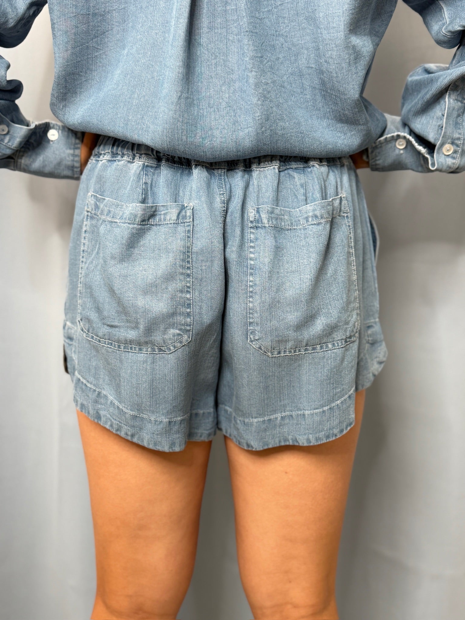 Person wearing a matching denim outfit with shorts and shirt on a plain background