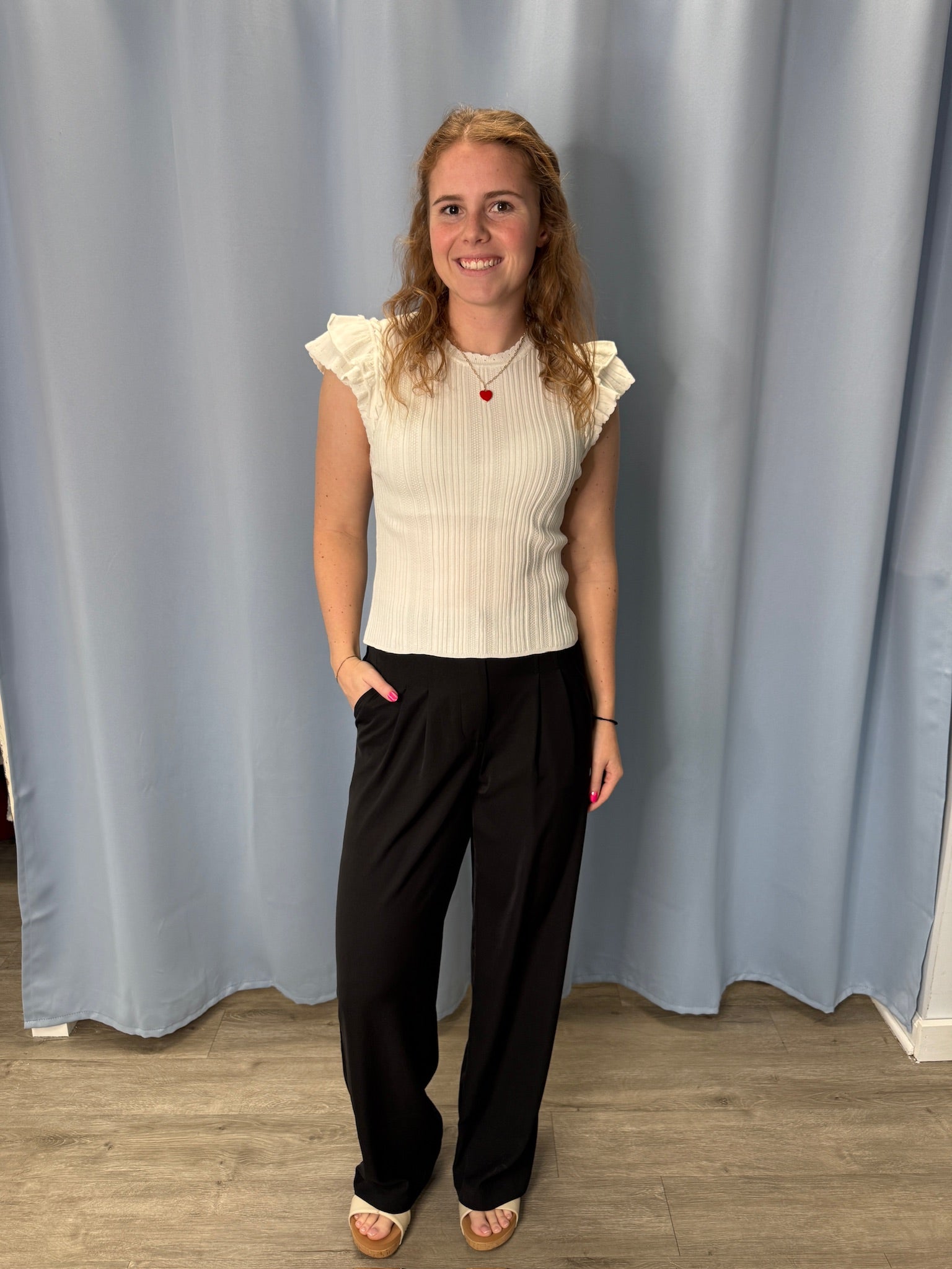 Woman wearing a white top and black pants standing in front of a gray curtain