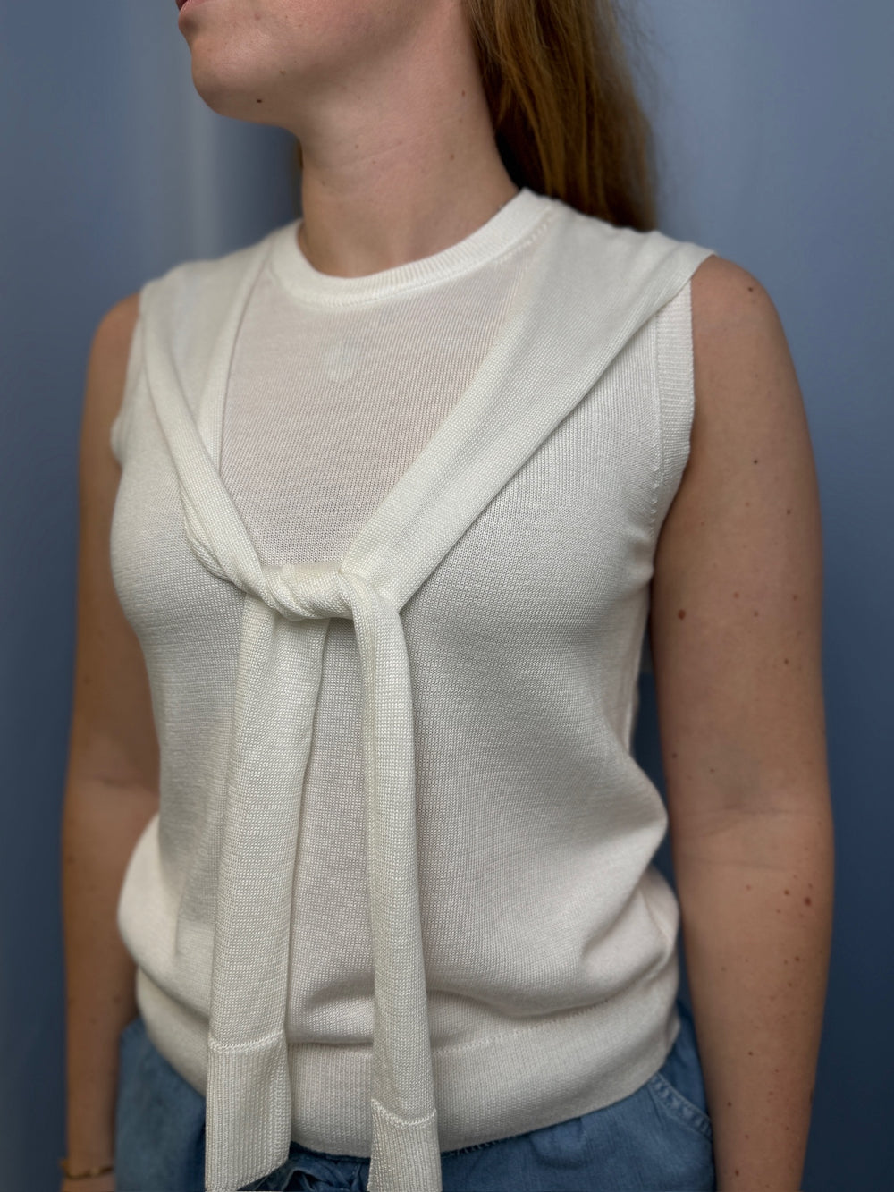 Woman wearing a white sleeveless top with a tie detail against a blue background