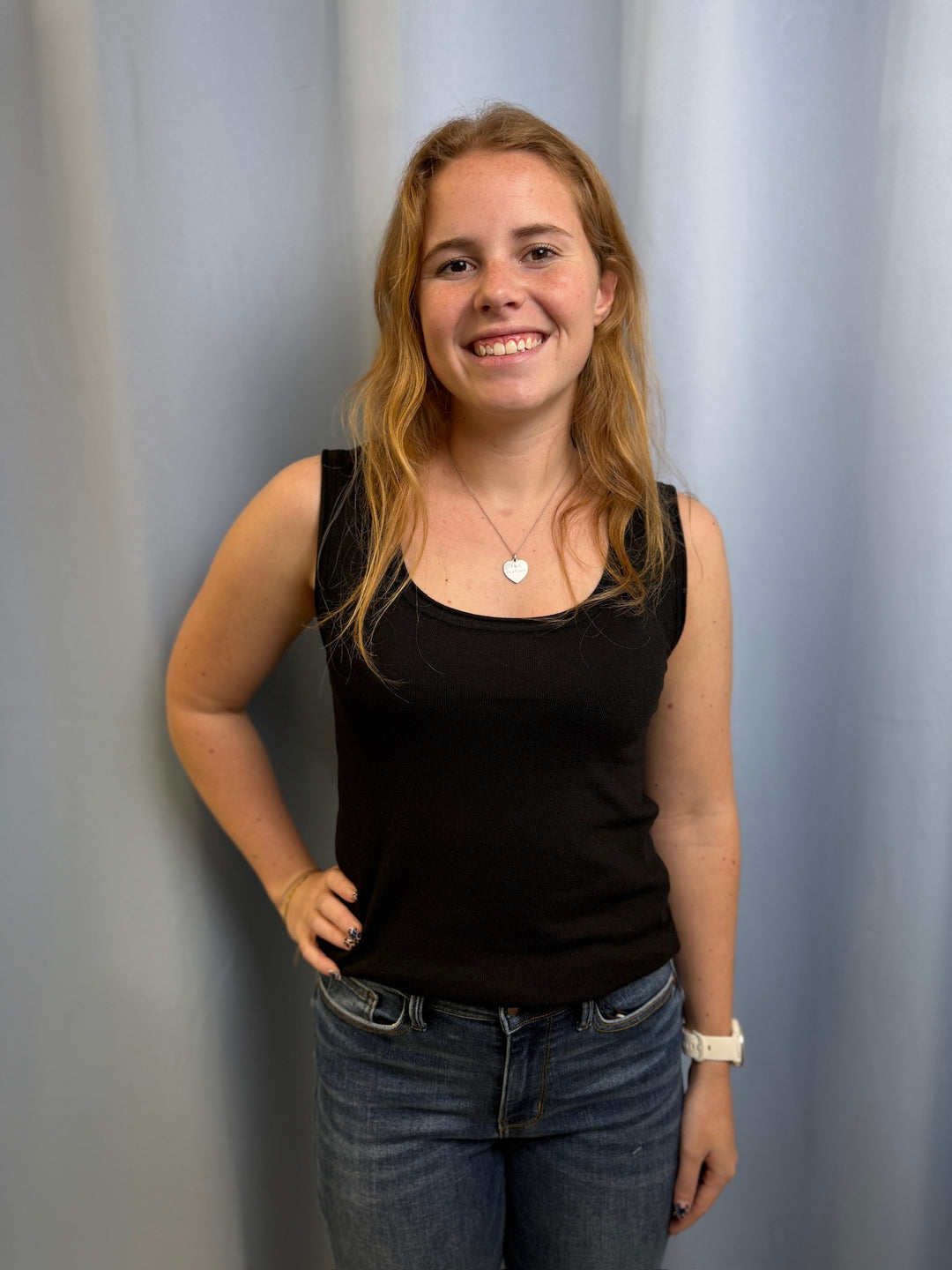 Woman wearing a black tank top and blue jeans against a plain background