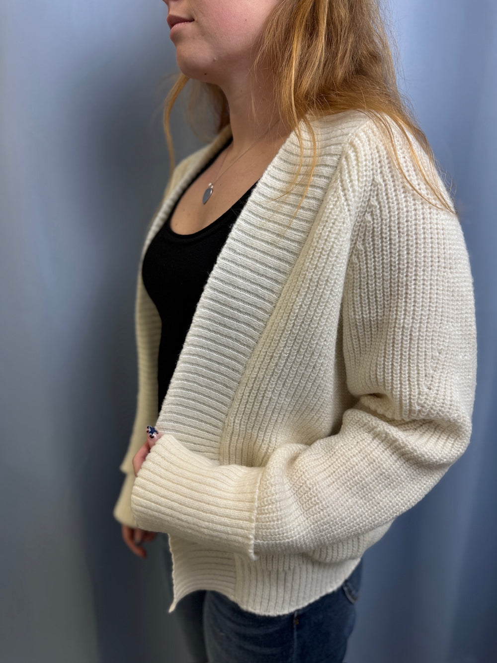 Person wearing a cream ribbed cardigan against a plain background