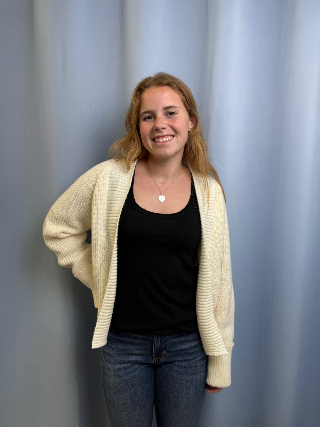 Woman wearing a beige cardigan over a black top with a plain background