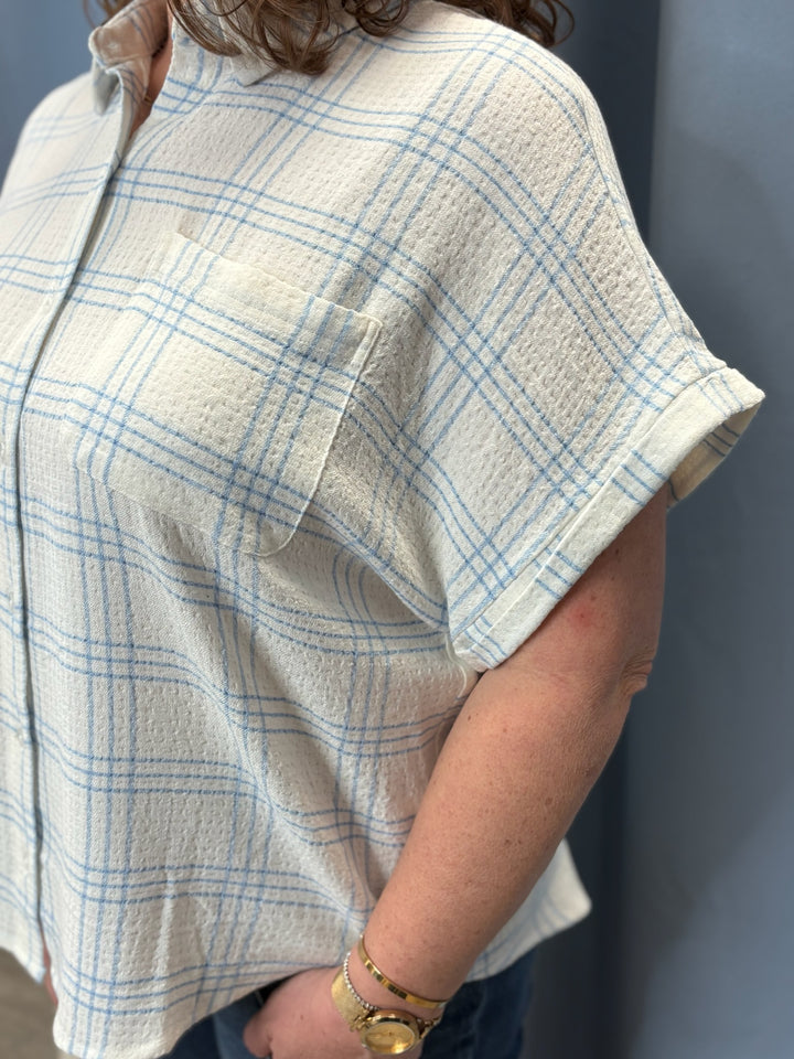 Person wearing a beige and blue plaid shirt against a gray background