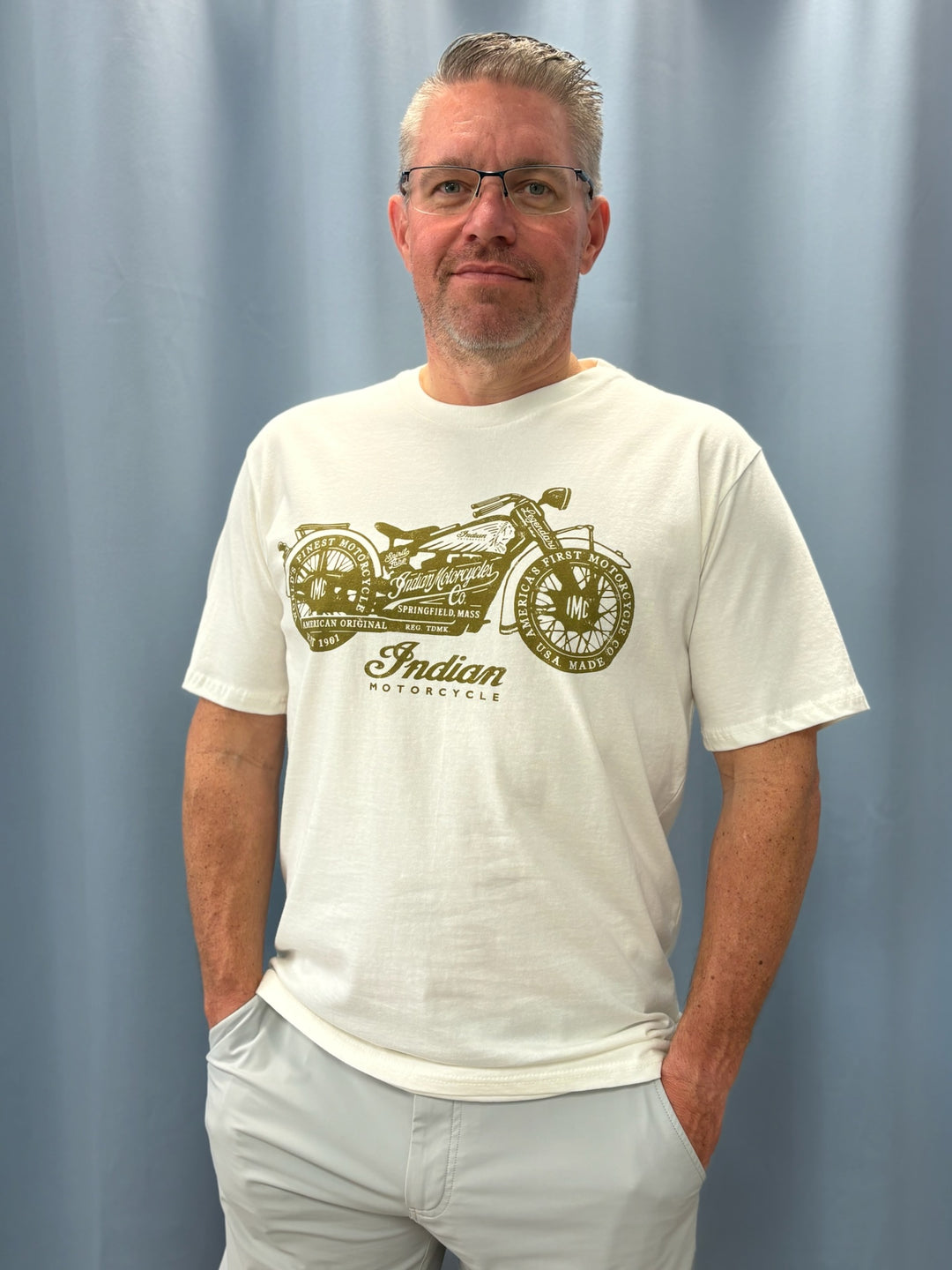 Man wearing a white t-shirt with an Indian Motorcycle graphic against a plain background