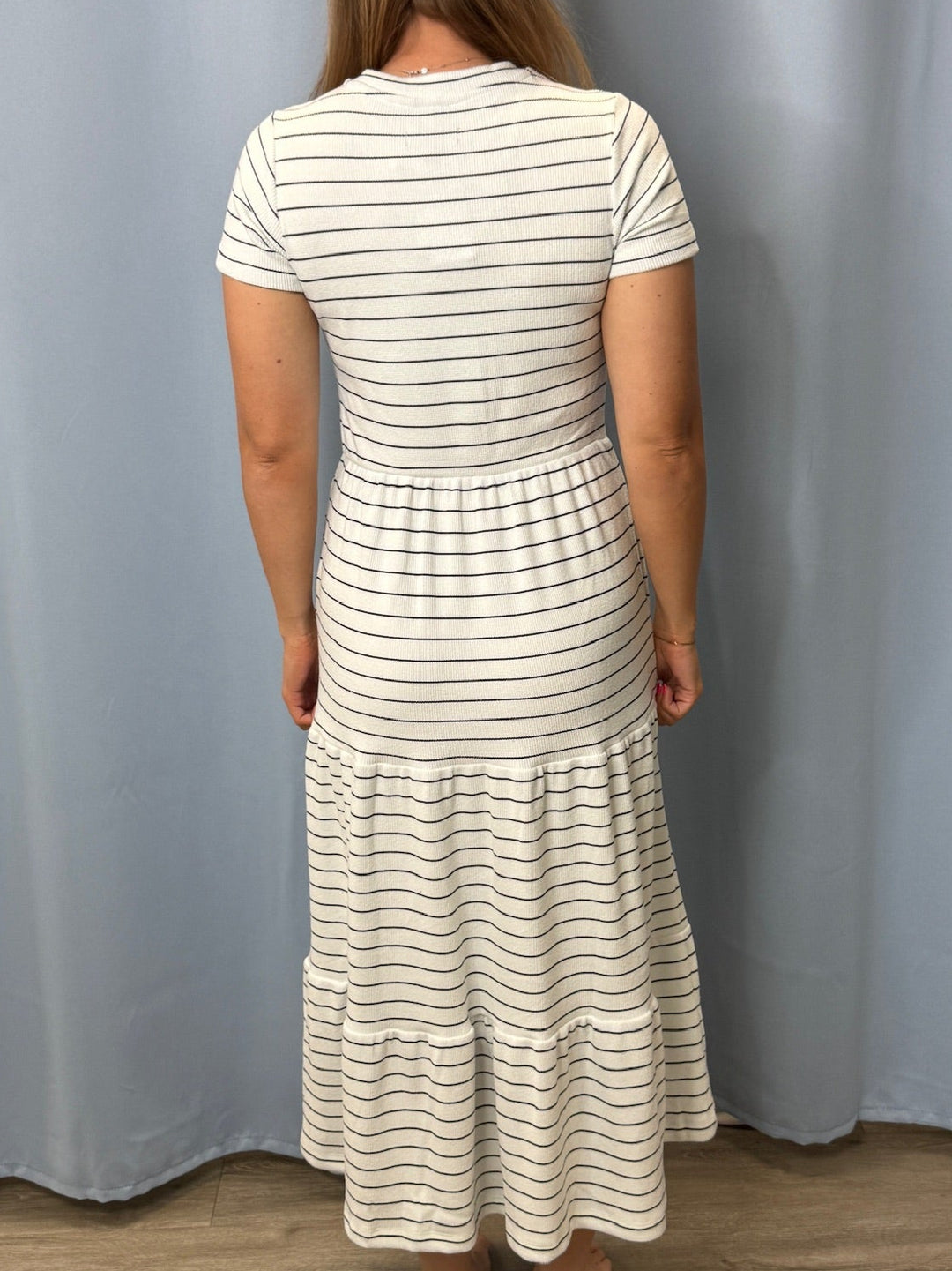 Woman wearing a white and black striped dress standing against a plain background
