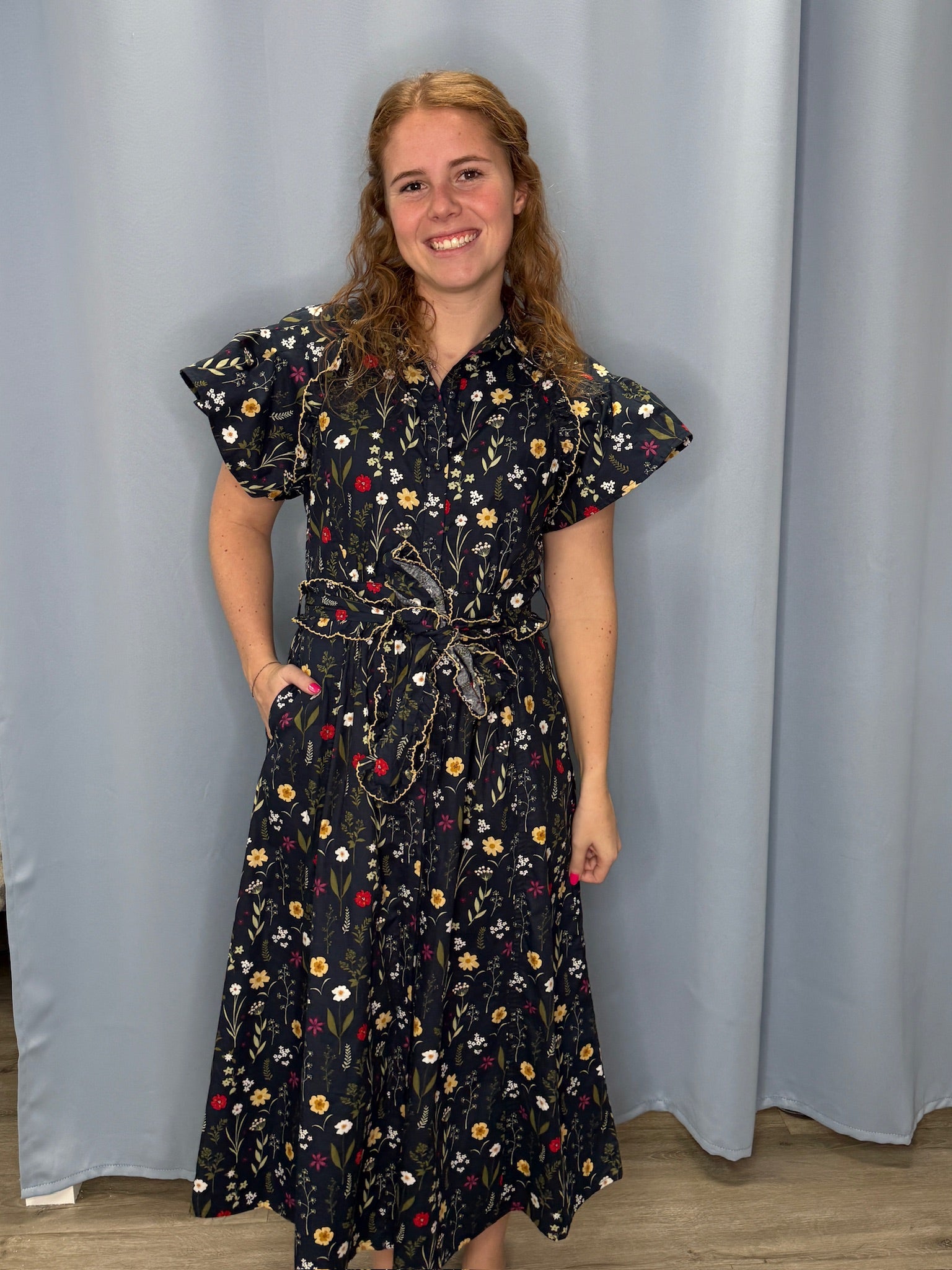 Woman wearing a black floral dress standing against a plain background