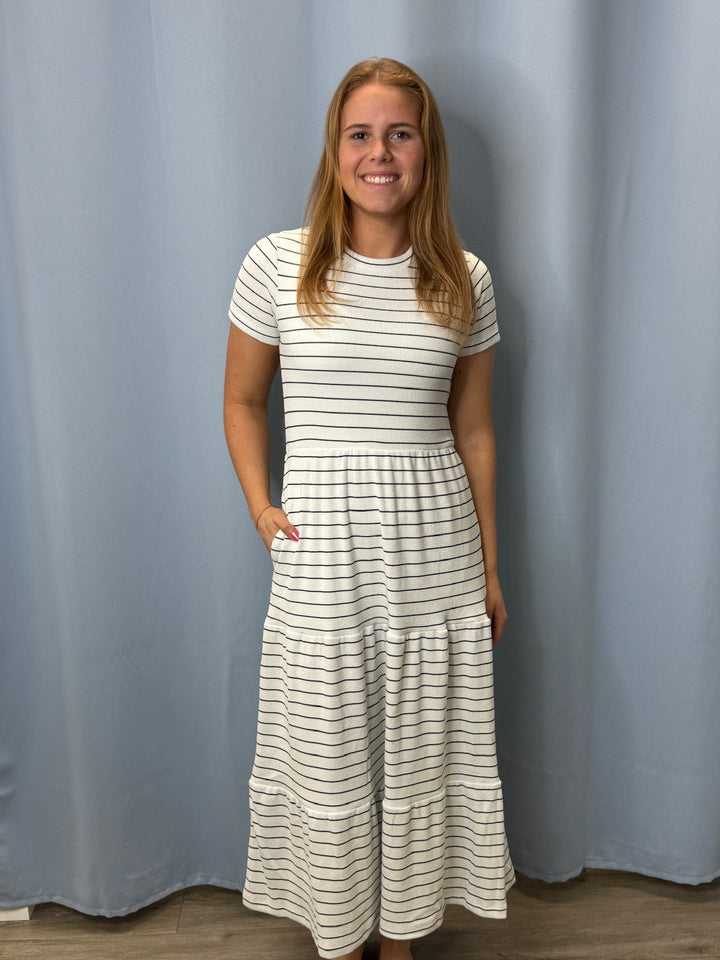 Woman wearing a long, white dress with black stripes against a plain background