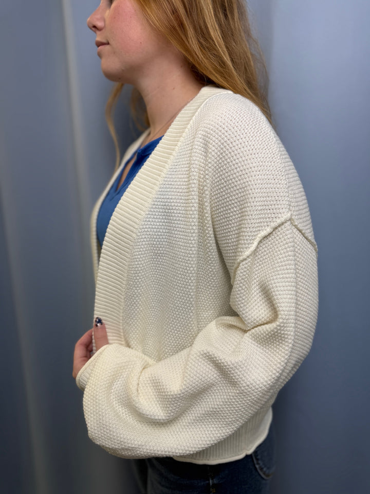 Person wearing a cream cardigan over a blue top against a plain background