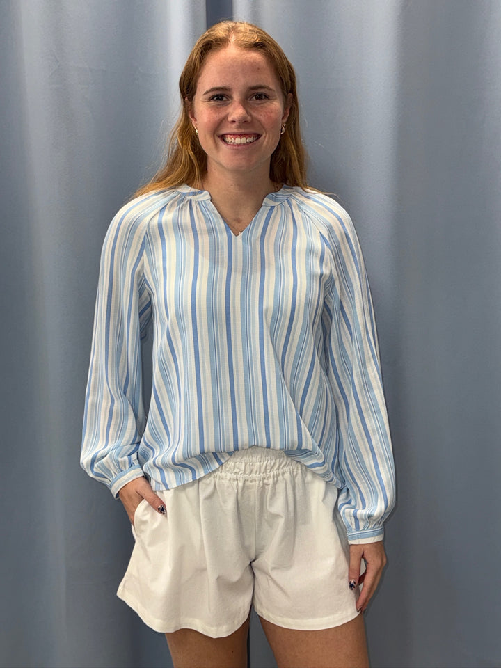 Woman wearing a blue and white striped shirt and white shorts against a gray curtain background