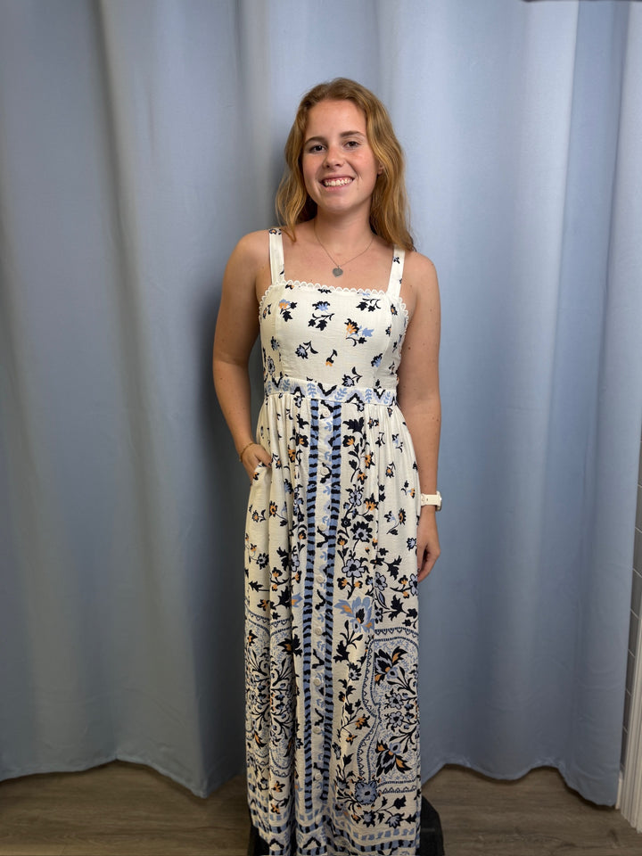 Woman wearing a floral dress standing against a plain curtain background