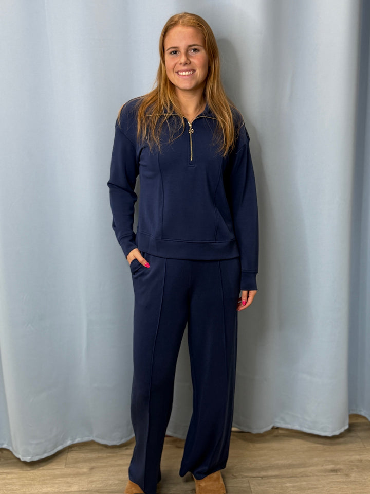 Person wearing a navy blue outfit standing against a light gray curtain.