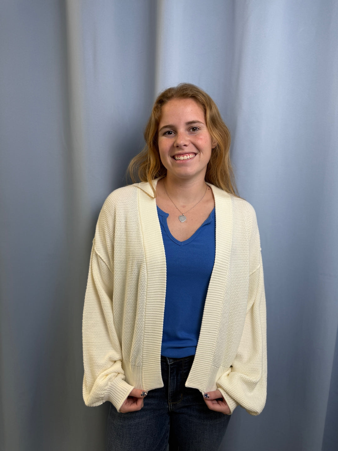 Woman wearing a white cardigan over a blue shirt against a plain background