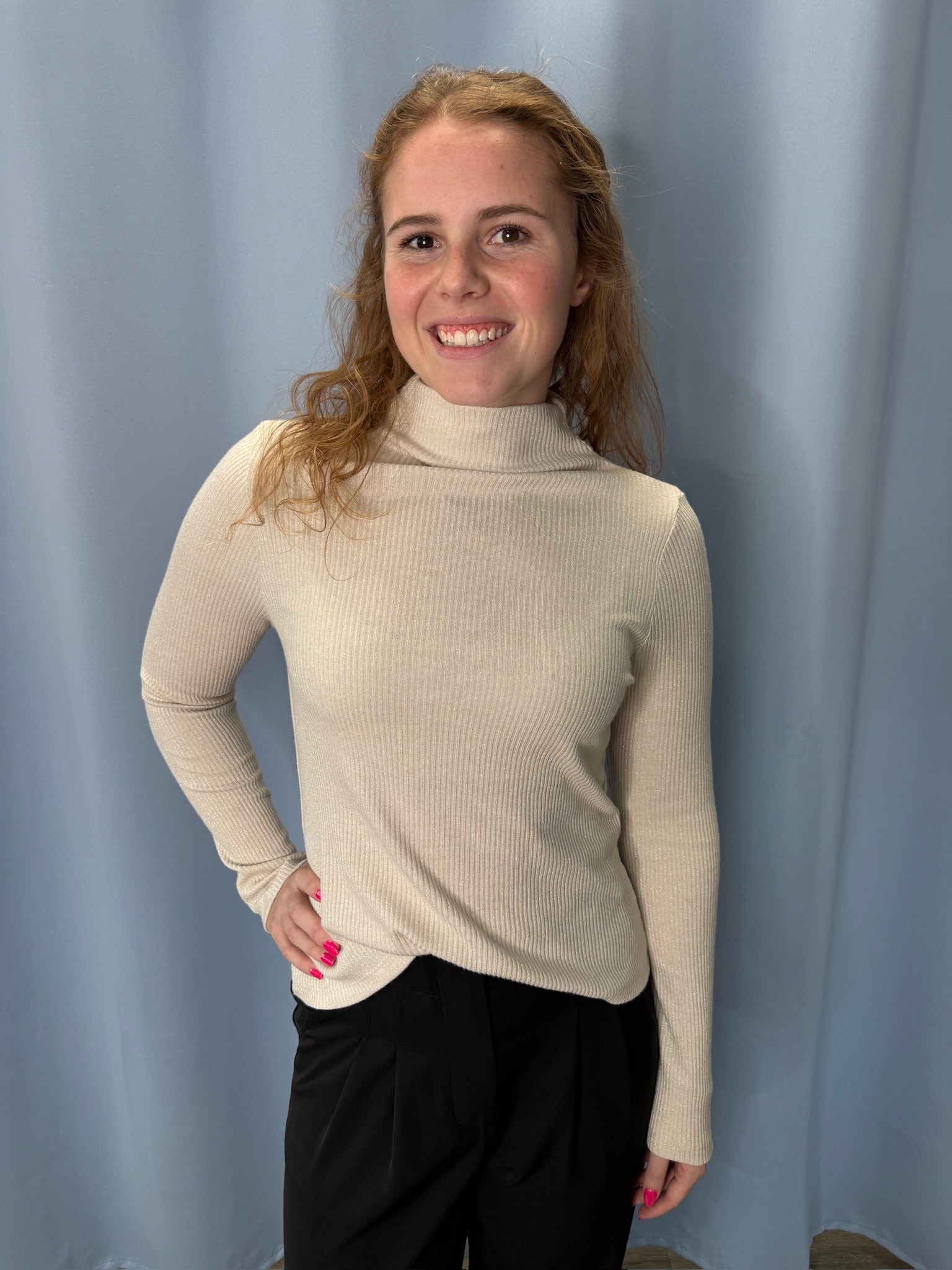 Person wearing a beige turtleneck sweater against a plain background