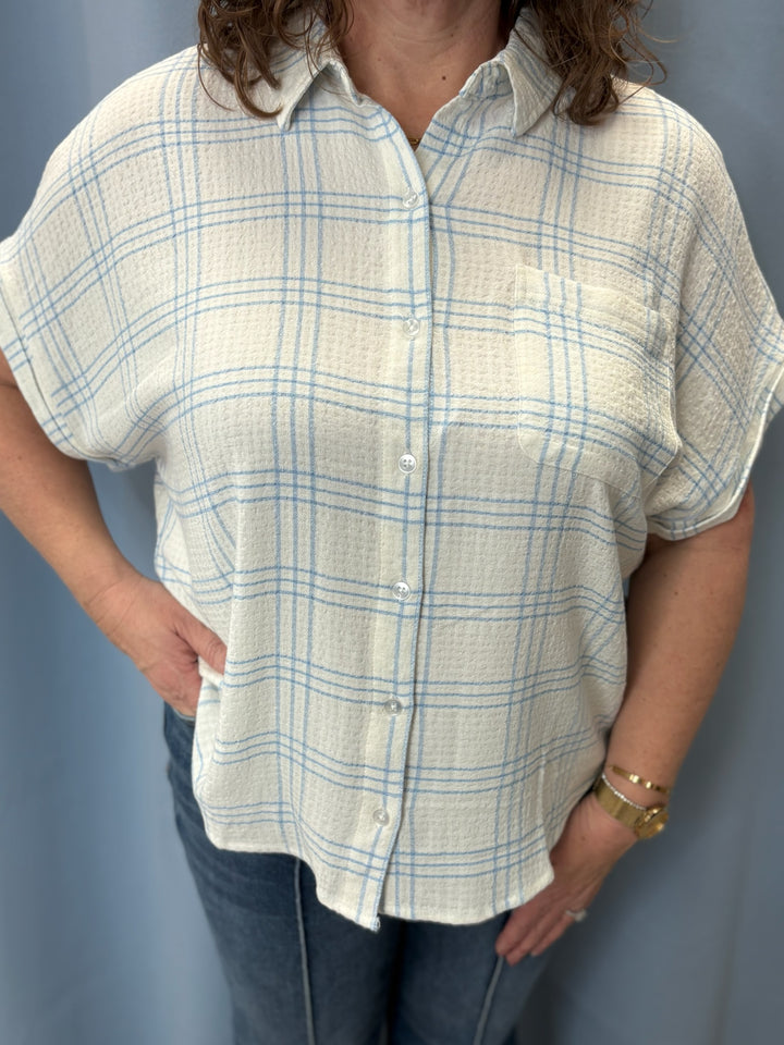 Person wearing a short-sleeve plaid shirt against a plain background