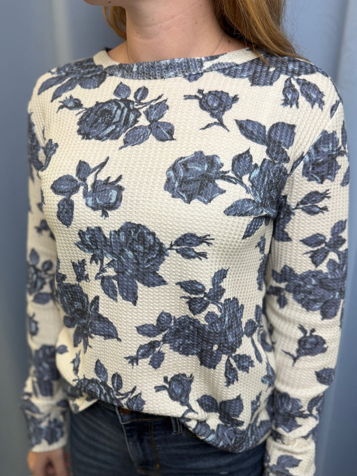 Person wearing a white sweater with blue floral patterns against a plain background