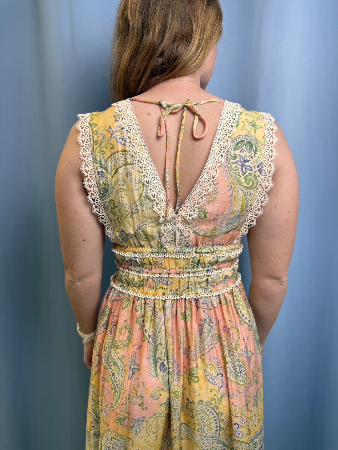 Woman wearing a colorful paisley dress with lace details against a blue background