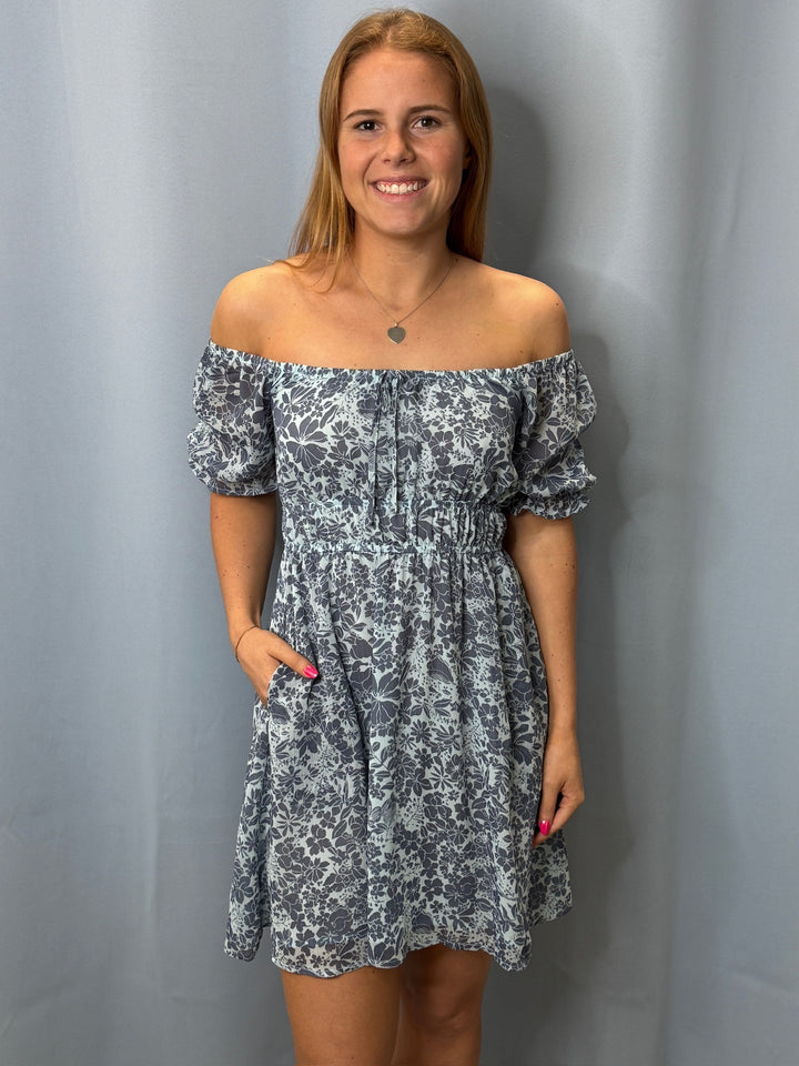 Woman wearing a floral off-shoulder dress against a plain background