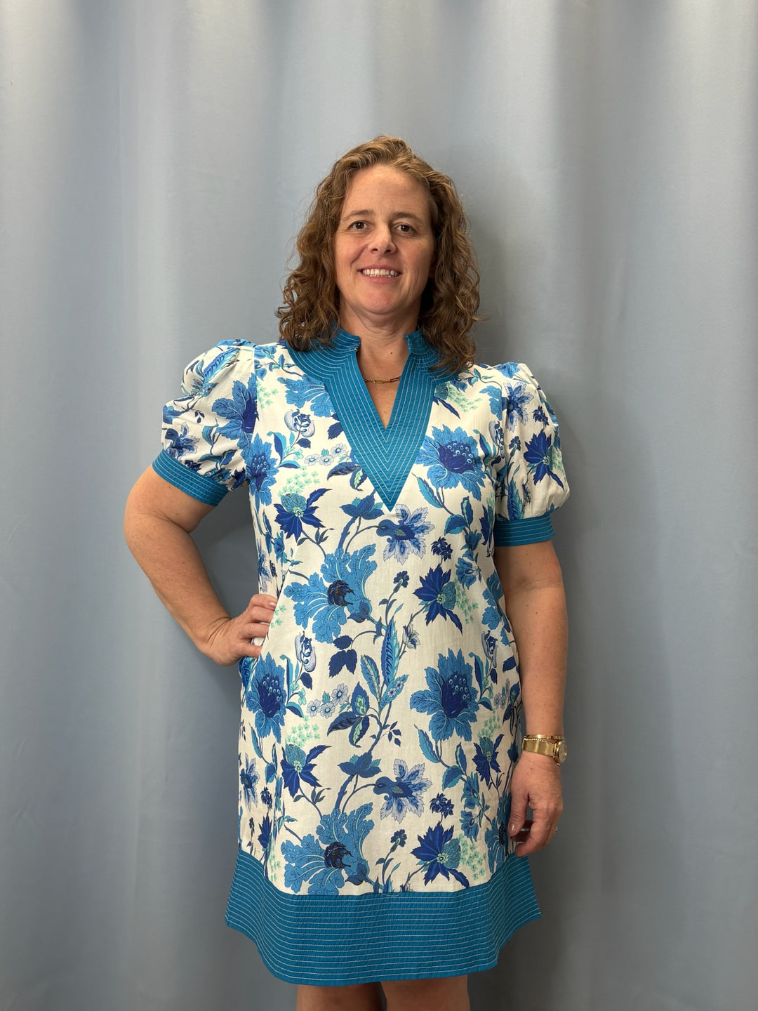 Woman wearing a floral dress with a blue and white pattern against a gray curtain background