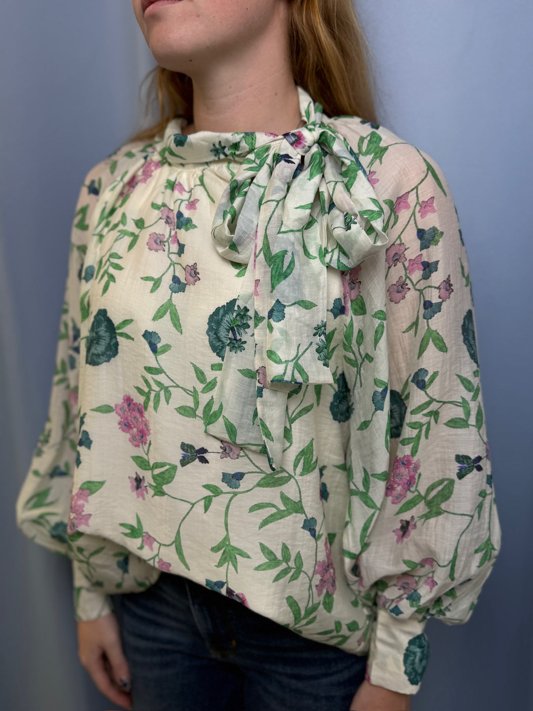 Woman wearing a floral blouse with a bow tie against a plain background