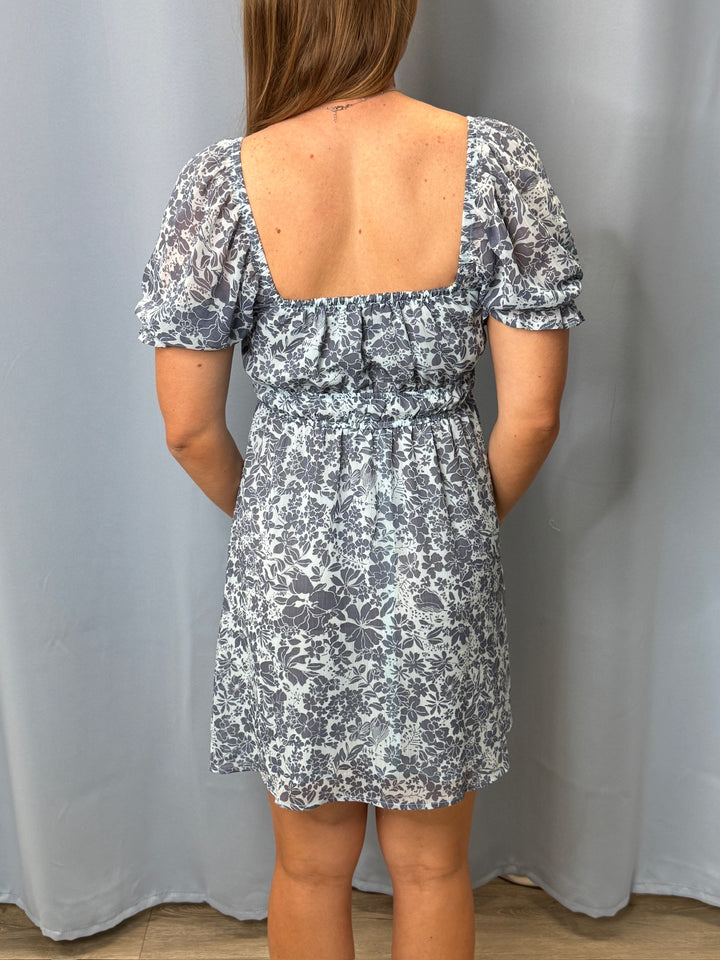 Person wearing a floral dress with an open back against a plain background