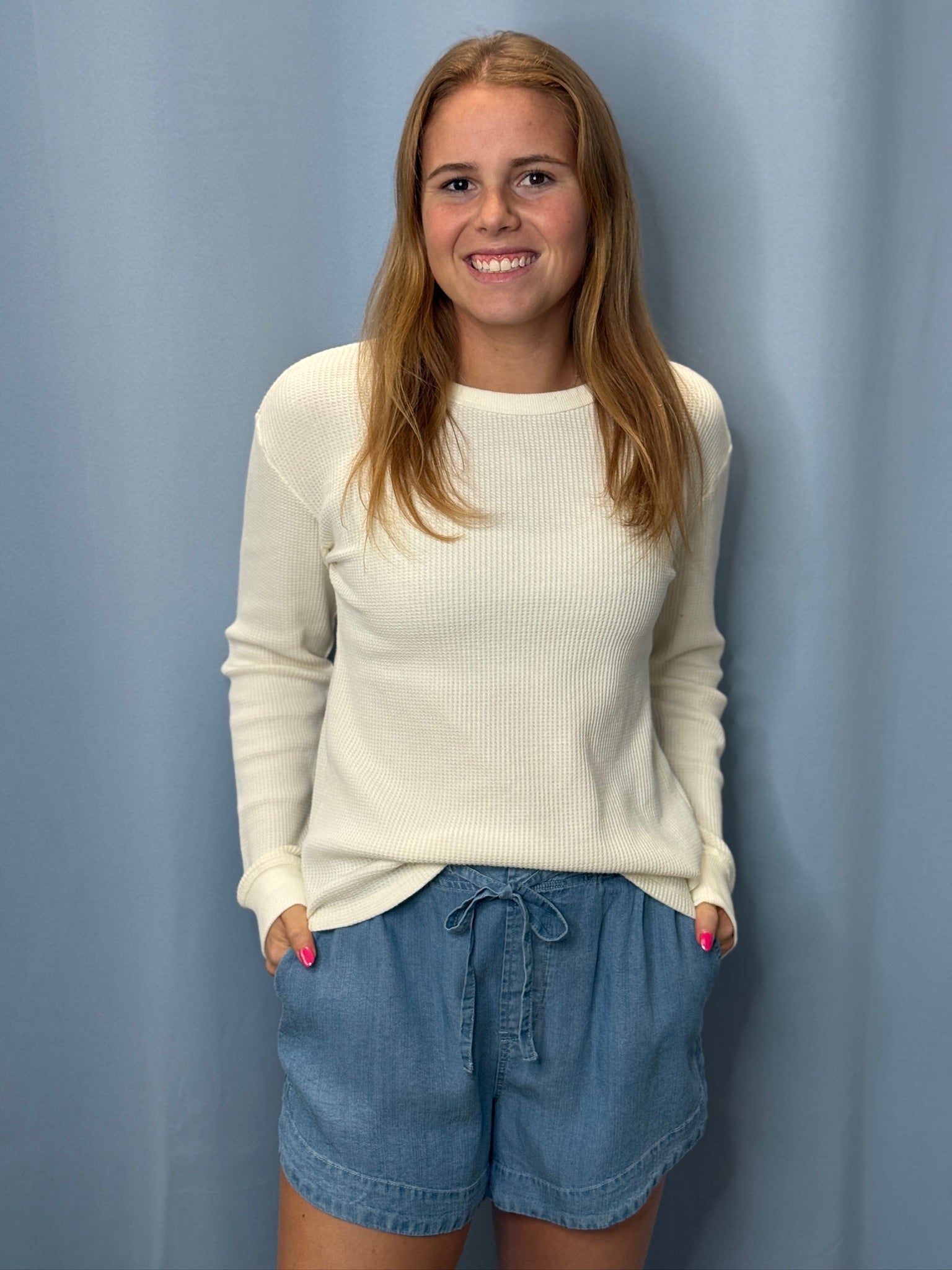 Woman wearing a white sweater and blue shorts against a light blue background