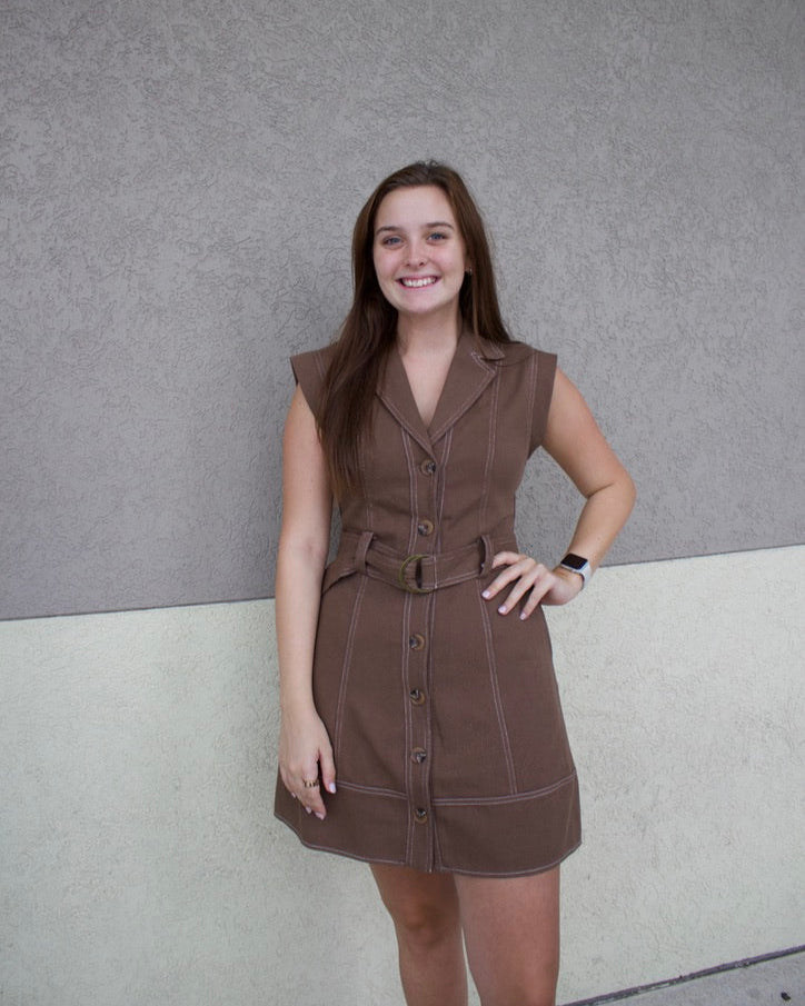 Woman wearing a brown dress against a gray wall