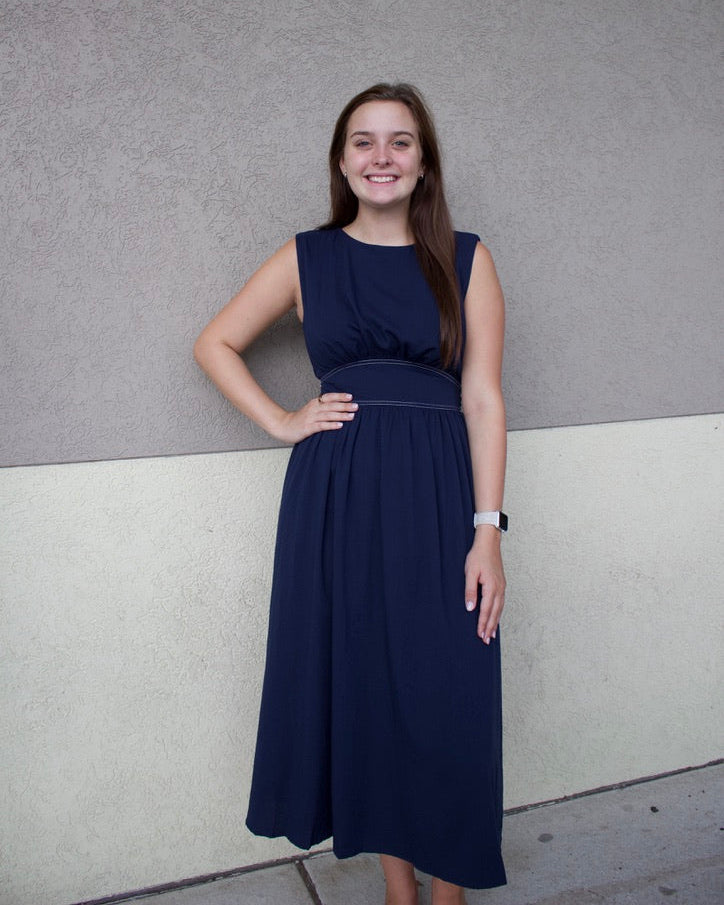 Woman in a navy blue dress standing against a gray wall.
