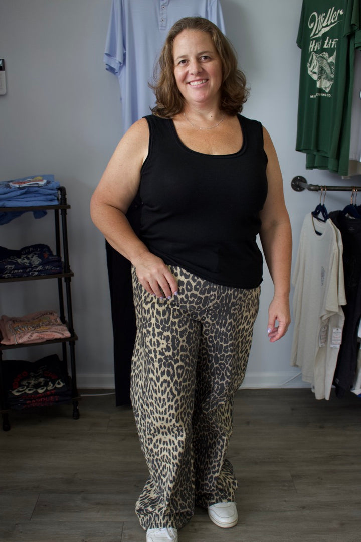 Woman wearing a black tank top and leopard print pants standing in a room with clothes on shelves.