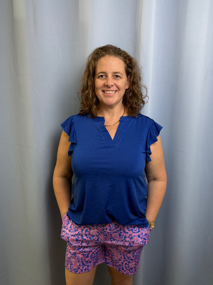 Woman wearing a blue top and pink floral shorts standing against a plain background