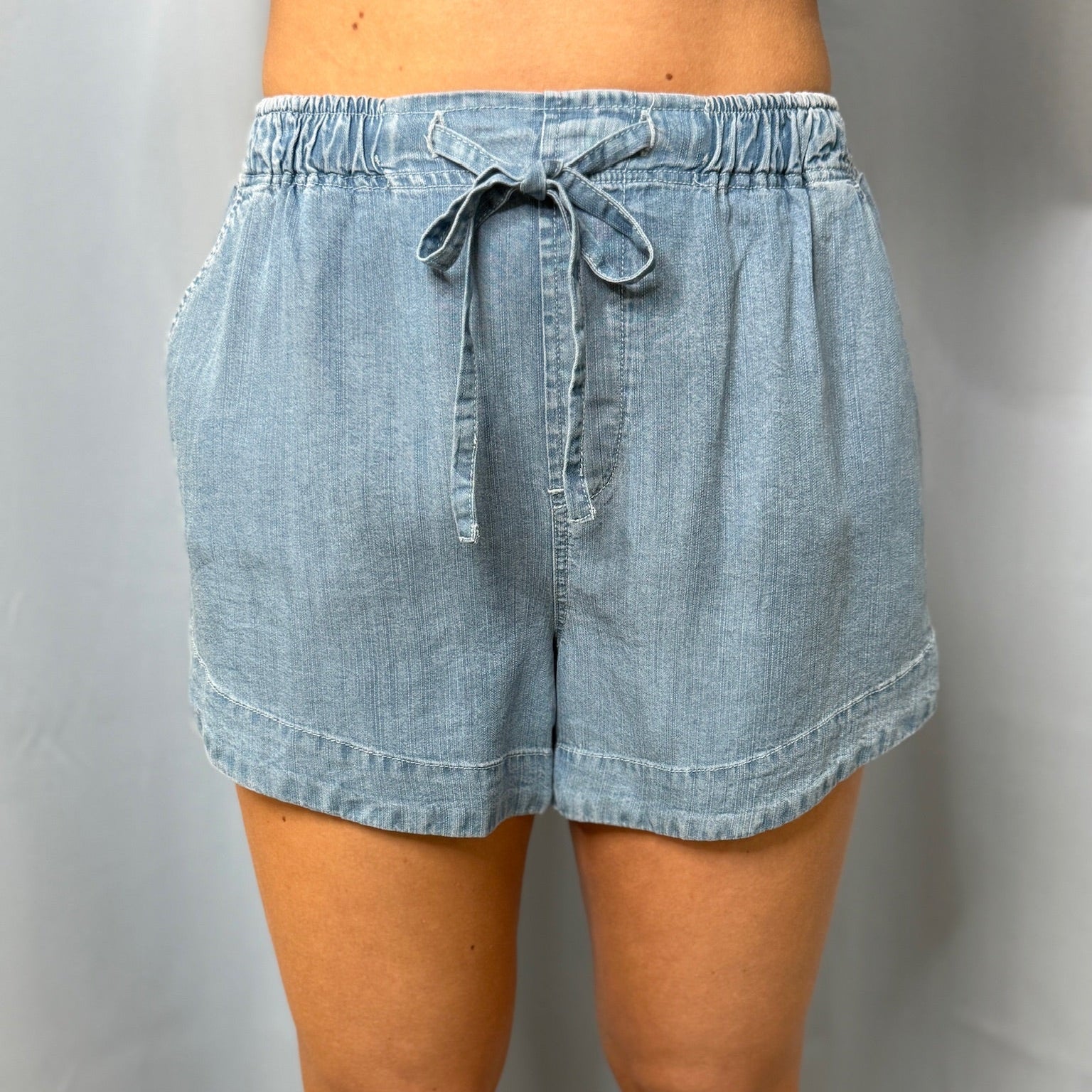 Light blue denim shorts with a tie waist on a plain background