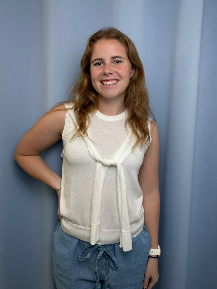 Woman wearing a white sleeveless top and blue pants against a plain background