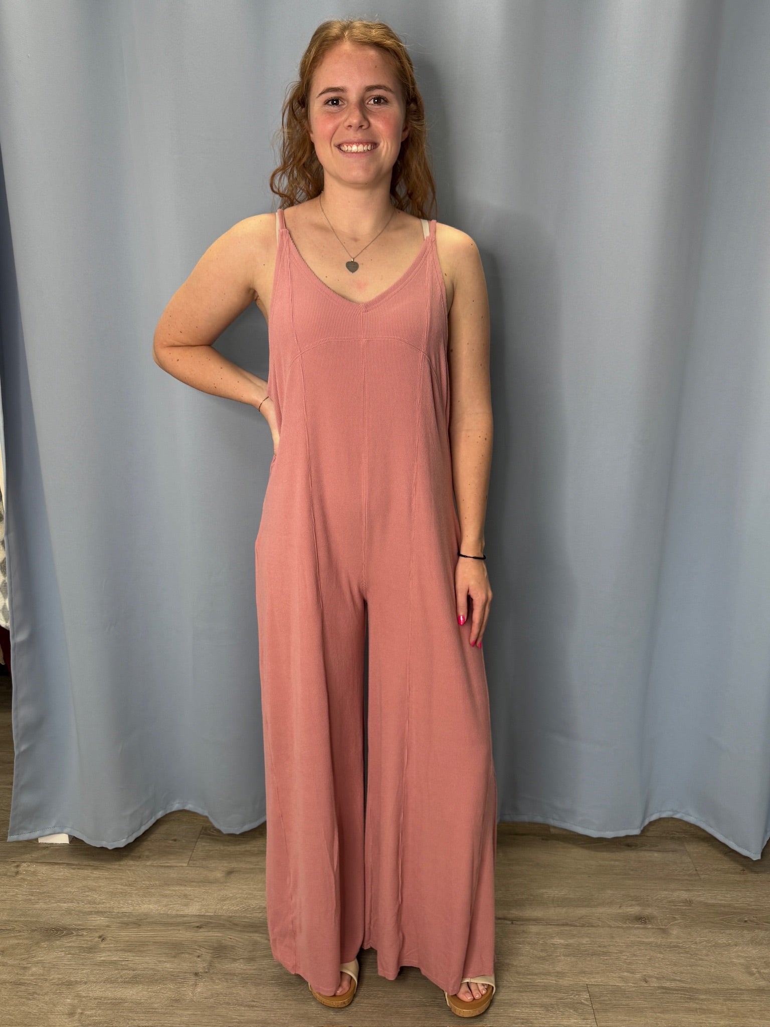 Woman wearing a pink jumpsuit standing against a plain background