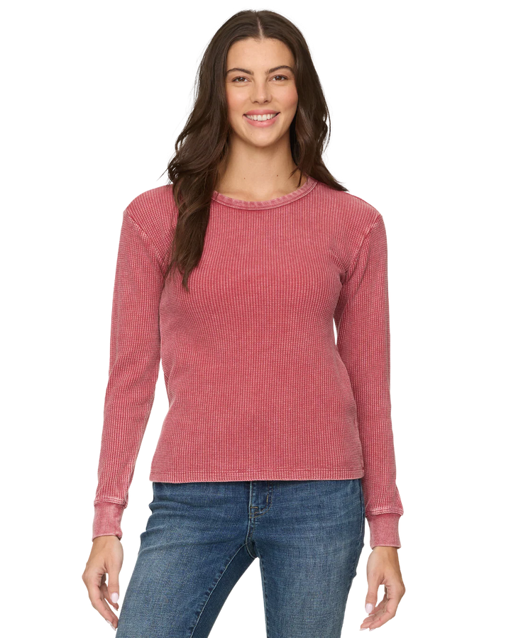 Woman wearing a pink ribbed long-sleeve top and blue jeans on a white background