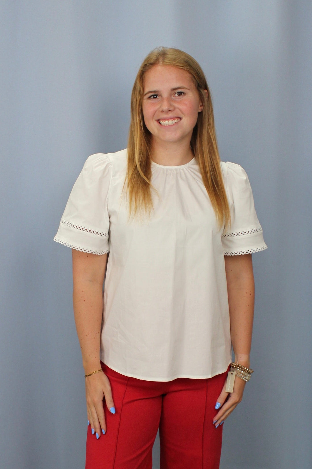 Woman wearing a white blouse and red pants standing against a plain background