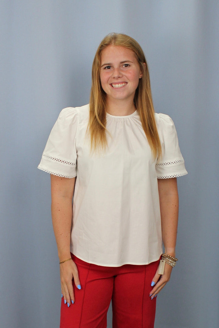Woman wearing a white blouse and red pants standing against a plain background