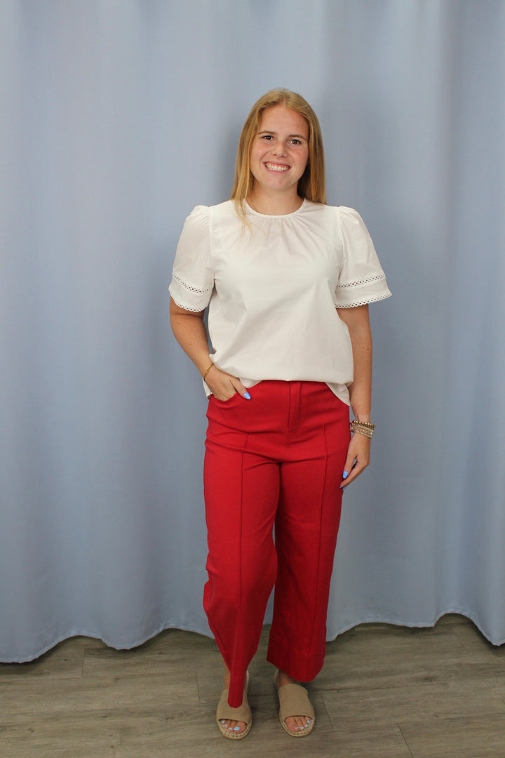 Woman wearing a white blouse and red pants standing against a plain background