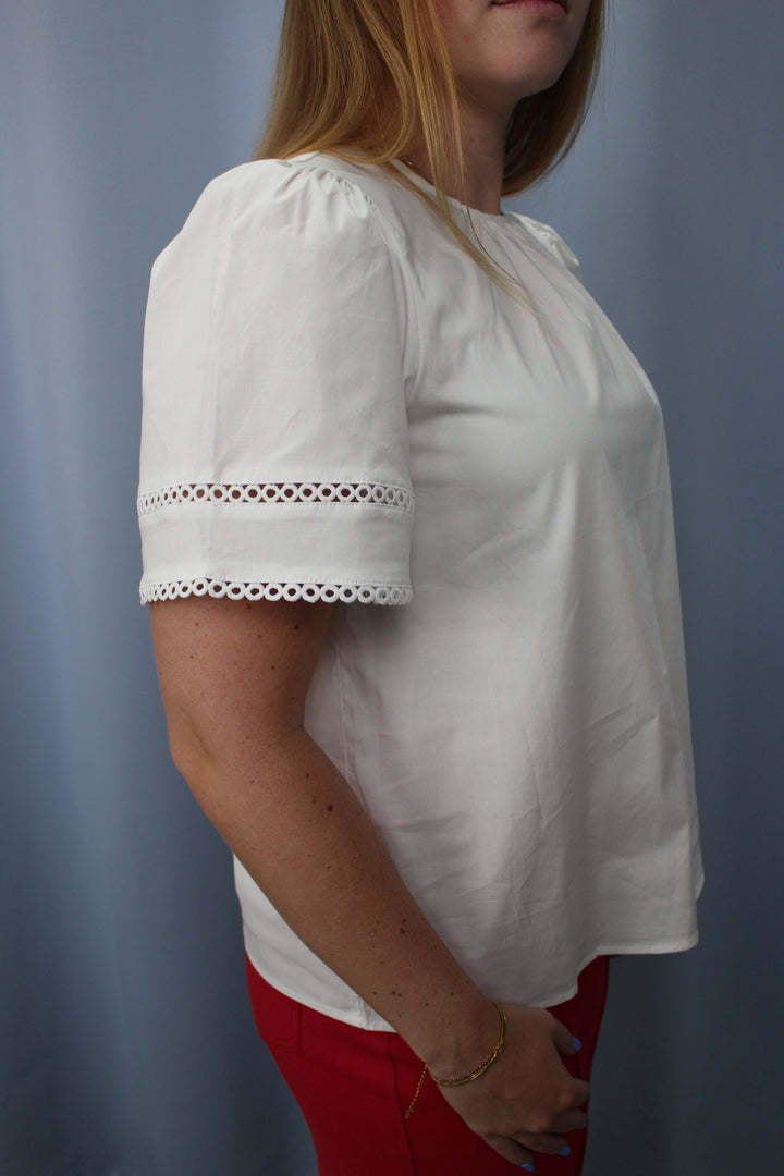 Woman wearing a white blouse with lace trim on a plain background